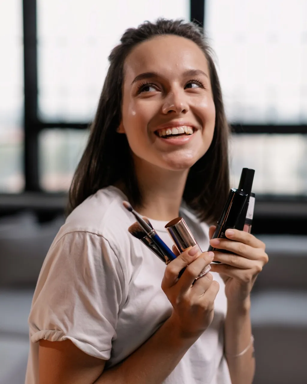 Mujer sonriente con brochas, labial y productos de maquillaje en la mano — cosmética y perfumería para distribuidores que venden por mayor con su tienda B2B VentasxMayor